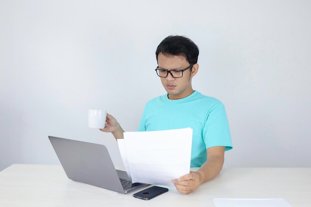 Wow face of Young Asian man shocked what he see in the document when working with laptop isolated grey background wearing blue shirt