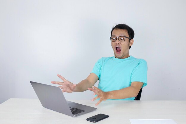 Wow face of Young Asian man shocked what he see in the laptop when working isolated grey background wearing blue shirt