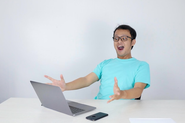 Wow gezicht van jonge Aziatische man geschokt door wat hij op de laptop ziet tijdens het werken op een geïsoleerde grijze achtergrond met een blauw shirt