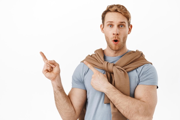 Wow impressive Excited redhead man gasping and looking amazed with promo offer pointing at upper left corner product promotional text showing advertisement white background