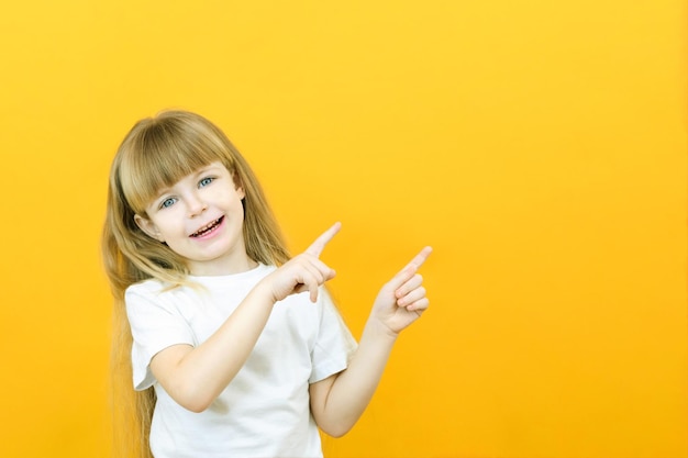 Wow kijk, adverteer hier Portret van een verbaasd schattig meisje wijzend op een lege ruimte op de achtergrond een peutermeisje op een gele achtergrond