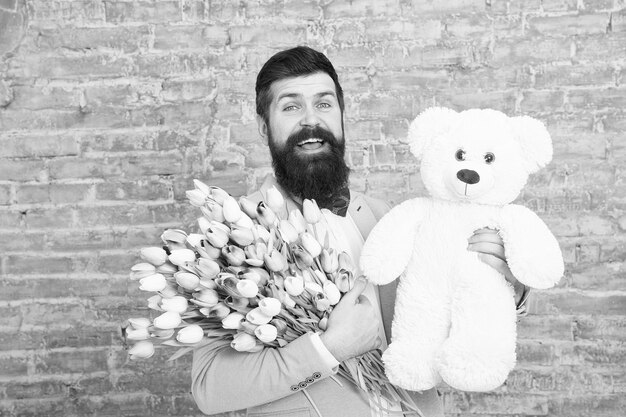 Wow Love date international holiday Spring gift Bearded man hipster with flowers Bearded man with tulip bouquet and bear Flower for March 8 Womens day Natural beauty Capturing a happy moment