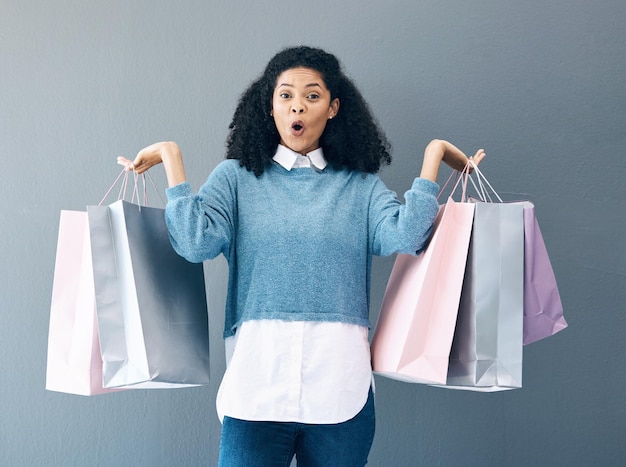 Wow sale and portrait of woman with shopping bags retail therapy and surprise at gift on a wall Deal excited and happy girl holding products from a shop market or mall on a grey background