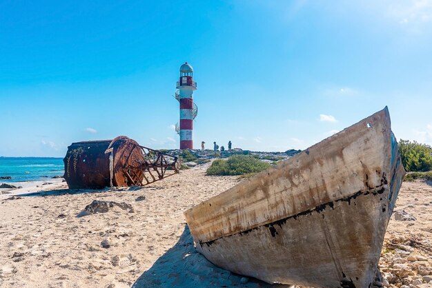 Wrak van nautische boei en boot op strand met toerist rond vuurtoren