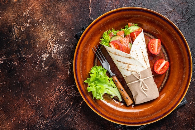 Wrap roll sandwich with fish salmon and vegetables. Dark background. Top view. Copy space.