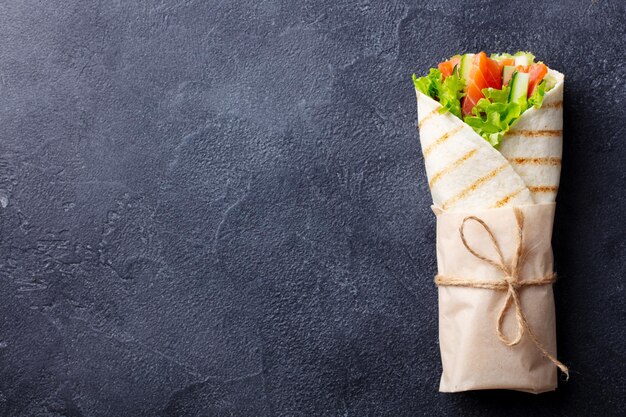 Фото Оберните сэндвич-ролл с рыбным лососем и овощами темный фон копией пространства вид сверху
