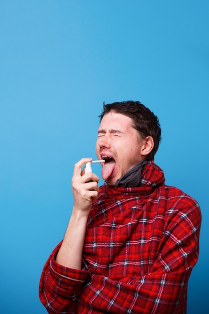 A wrapped in a blanket sick man is using spray with medicine for throat