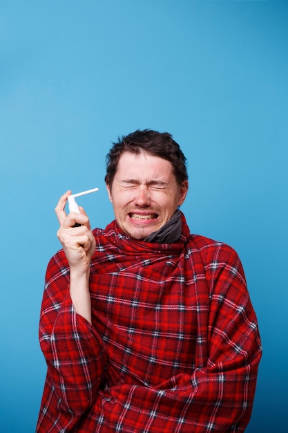 A wrapped in a blanket sick man is using spray with medicine for throat