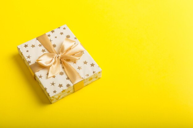 Wrapped christmas or other holiday handmade present in white paper with gold ribbon on colored background present box decoration of gift on colored table top view with copy space