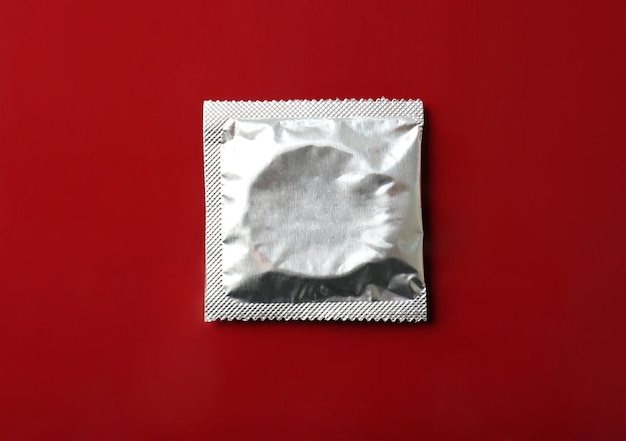 Wrapped condom on burgundy background Safe sex concept