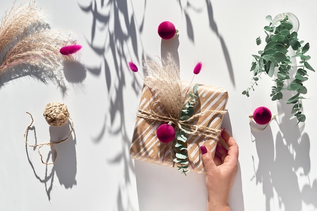 Wrapped gift box with natural Christmas decor in female hand. Eco friendly creative decorations - recycled craft wrapping paper, dry pampas grass, fresh natural eucalyptus twigs and dried bunny tails.