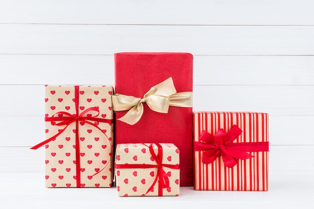 Wrapped gifts boxes with red ribbon on white wooden background.