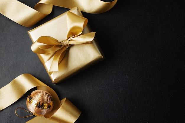 Wrapped golden gift with golden bow and baubles on black. Flat Lay.