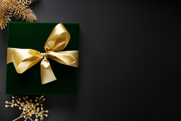 Wrapped golden gift with golden bow and baubles on dark backgrounds.