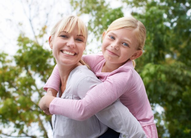 Photo wrapped in my daughters love a happy young mother givign her daughter a piggyback ride in the park
