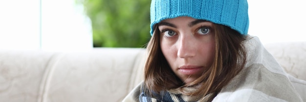 Wrapped young woman is sitting in hat and in plaid with pill