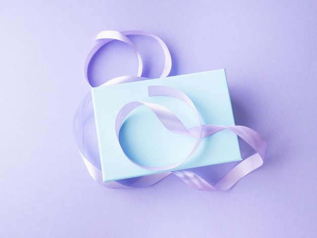 Wrapping blue pastel present box with ribbon on purple background