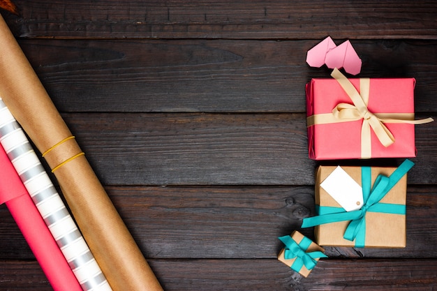 Wrapping paper, wrapped gifts and small hearts on a dark wooden table. View from above.