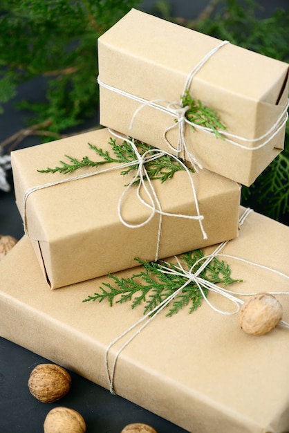 Wrapping rustic eco Christmas packages with brown paper, string and natural fir branches on dark background