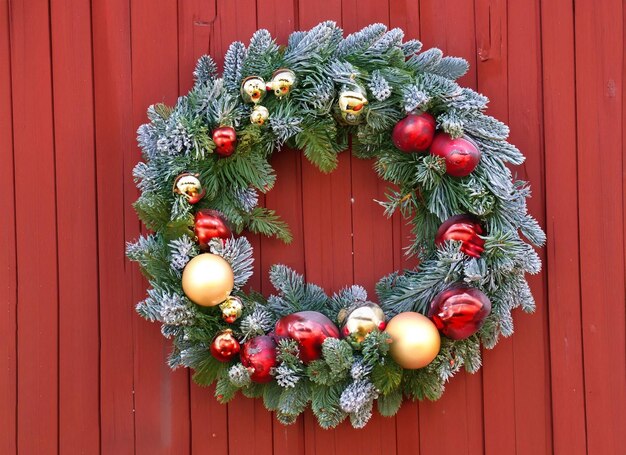 Wreath bound by green sprigs hanging on red wooden wall in winter