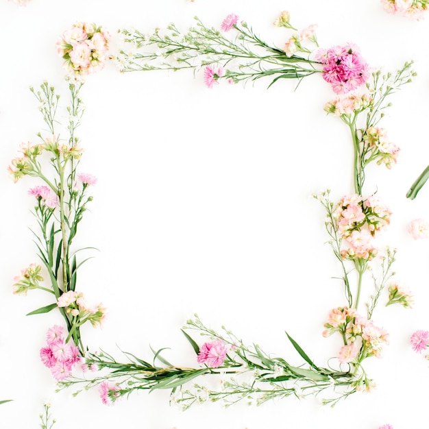 Wreath frame made of pink and beige wildflowers, green leaves, branches on white