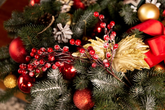 Corona fatta di rami e protuberanze dell'albero di natale, nastri rossi e bacche rosse, palline dorate e rosse