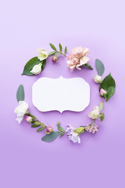 紫色の背景にバラのつぼみ、繊細な白い花、枝、葉、花びらを持つヴィンテージフレームの花輪。フラットレイアウト、上面図