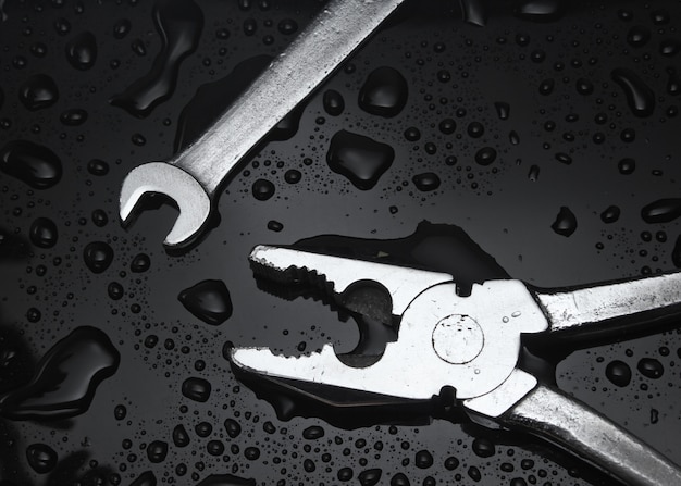 Wrench and pliers on black with water drops.