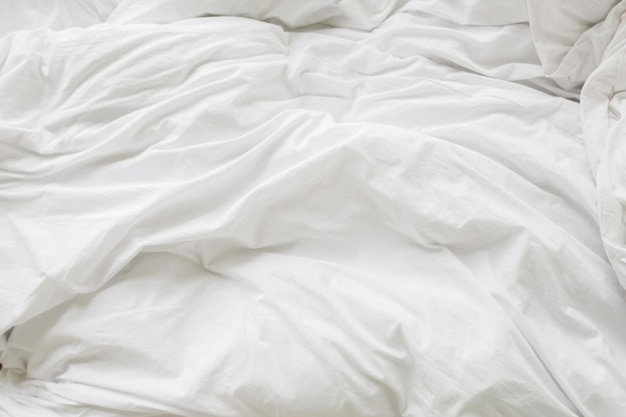 Фото Морщинистое грязное одеяло и белая подушка в спальне после пробуждения утром от сна в долгой ночи детали одеяла и одеяла неубранная кровать в спальне отеля с белым одеялом