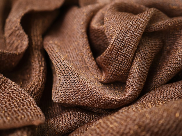 Wrinkled brown silk knitted fabric with gold threads as background Golden backdrop with curves luxury fashion Abstract crumpled brown and gold glittering texture Soft focus