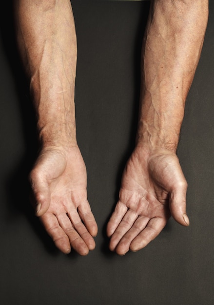 Photo wrinkled hands of an elderly man on a table close-up isolated on a black surface. top view.