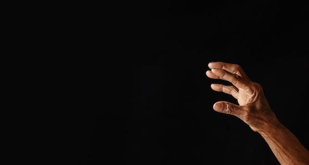 Wrinkled old man's hand with empty hand on dark background