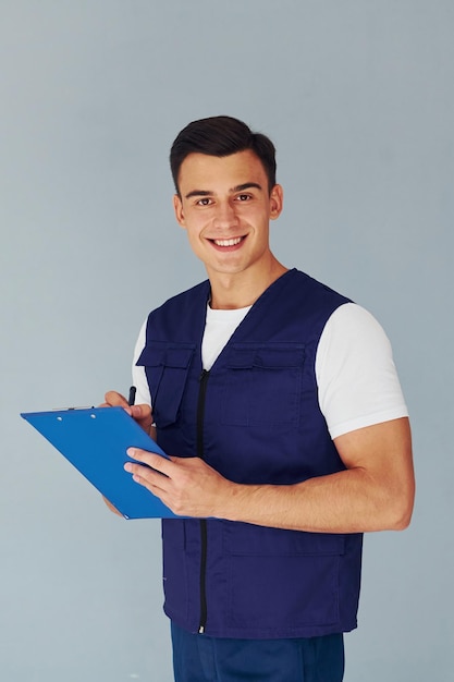 Writes in notepad Male worker in blue uniform standing inside of studio against white background