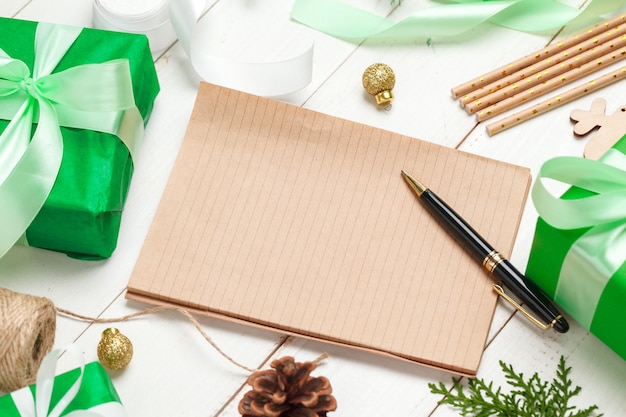 크리스마스 인사말 카드 작성. 장식 된 나무 테이블에 펜으로 메모장을 엽니 다