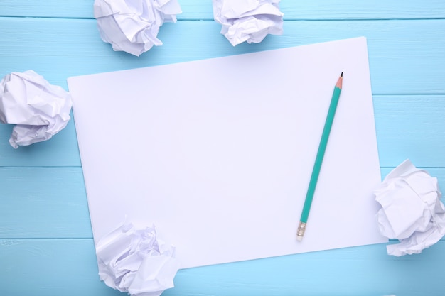 Writing concept - crumpled up paper wads with a sheet of white paper and pencil on blue wooden