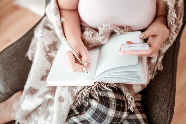 Writing in notebook. Good-looking woman in household outfit filling diary with metal slick pen