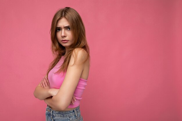 Wrokkige jonge mooie donkere blonde vrouw met oprechte emoties geïsoleerd op de achtergrondmuur met kopie ruimte stijlvolle roze top dragen. Negatief concept.