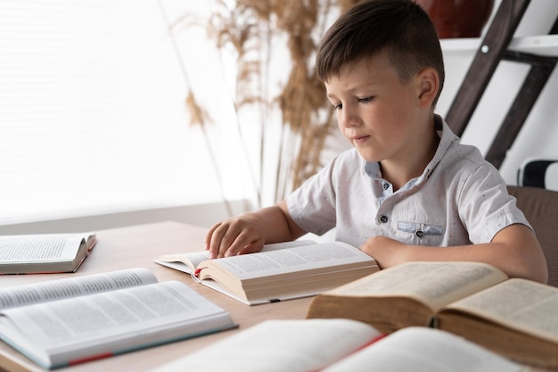 Wunderkind child sitting at the table in the library reads open books or textbooks in front of student does his homework knowledge from literature concept back to school