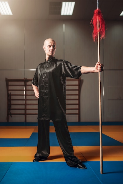 Wushu fighter poses with lance, martial arts. Man in black  cloth poses with blade