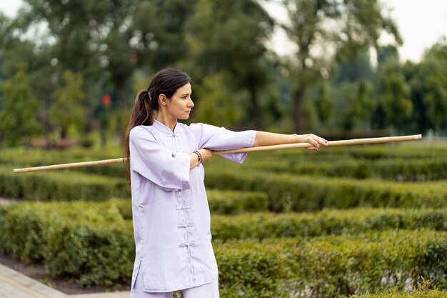 Wushu practice outdoors young lady fighter with stick in hands wearing kimono training at the summer park alone