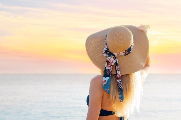 XABeautiful girl in a straw hat on the background of the sky with clouds and the sea Back view