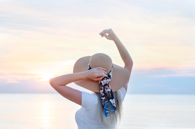 XA海沿いの夜明けの背景に帽子をかぶった幸せな女の子 背面図