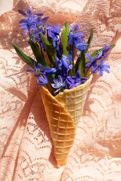 XASpring blauwe bloemen in een wafelkegel op een textielachtergrond met zonlicht