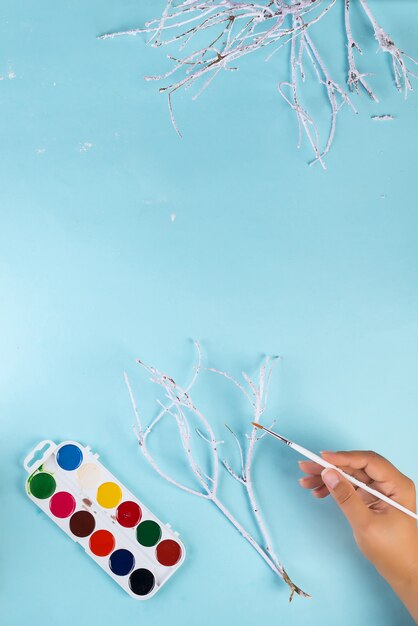 Xmas . Woman hand made of white painted branches for christmas decoration on blue , copyspace flat lay