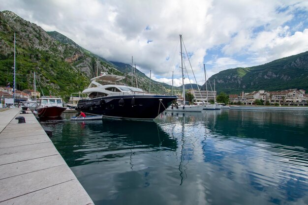 A yacht is docked in a marina with mountains in the background.