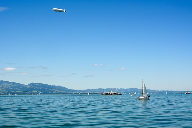 ヨットと船が明るいターコイズ ブルーの海の波の上を航行し、飛行船が空を飛んでいます。