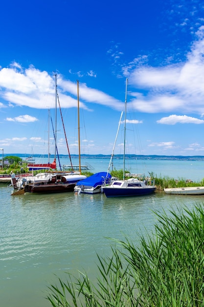 Yachts are moored to the shore of a lake with turquoise water