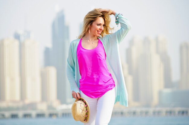 Yang European woman poses in stone fence in front of seaside modern city