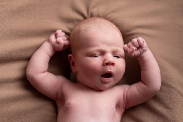 Yawning caucasian newborn baby yawning resting on brown blanket