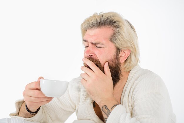 Yawning sleepy man with cup of coffee in hand coffee morning tired man in bed copy space for yours